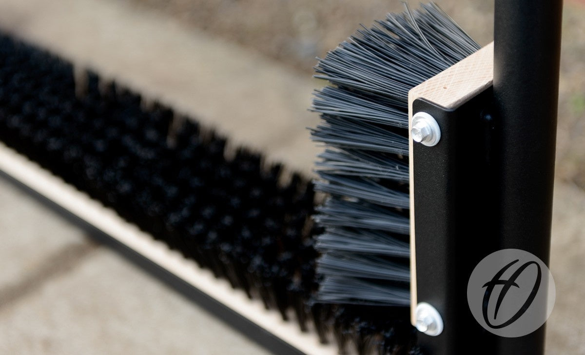 Close-up of the Harrod Sport Fixed Multi Boot Wiper, showing stiff black side brushes and a polyester powder coated steel wiper on metal frames for effective dirt removal. A concrete surface is visible in the blurred background.