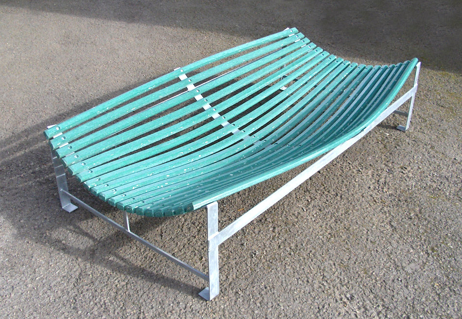 The Martin Berrill Sports Plastic Slip Catch Cradle features a curved green slatted design with a silver frame, set on a rough brown surface. Its durable structure bows inward to mimic professional fielding practice equipment.