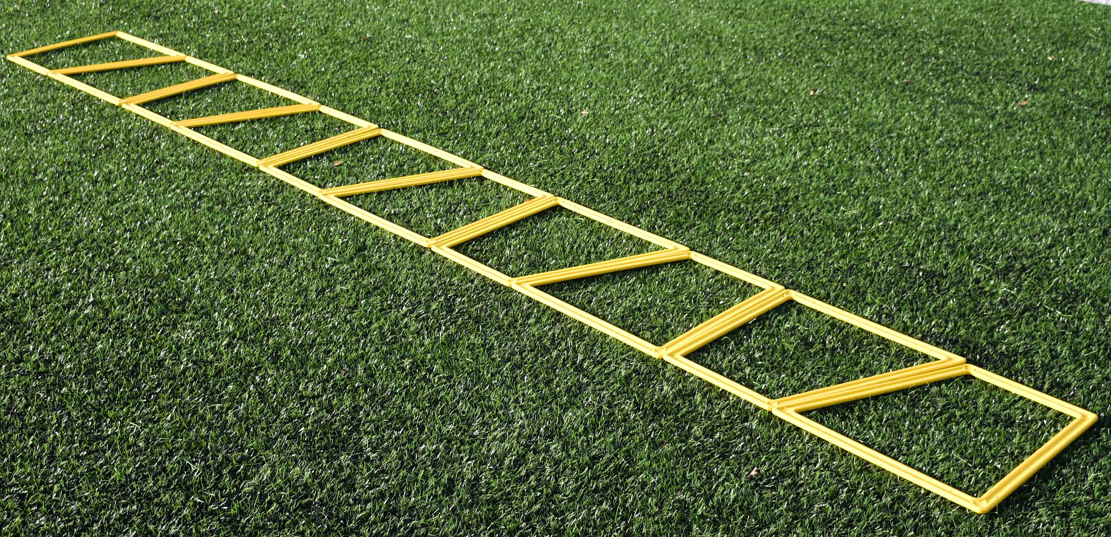 The Precision Training Precision Poly Grid System (set of 10) in yellow lies flat on green artificial grass, ideal for agility training and footwork drills.