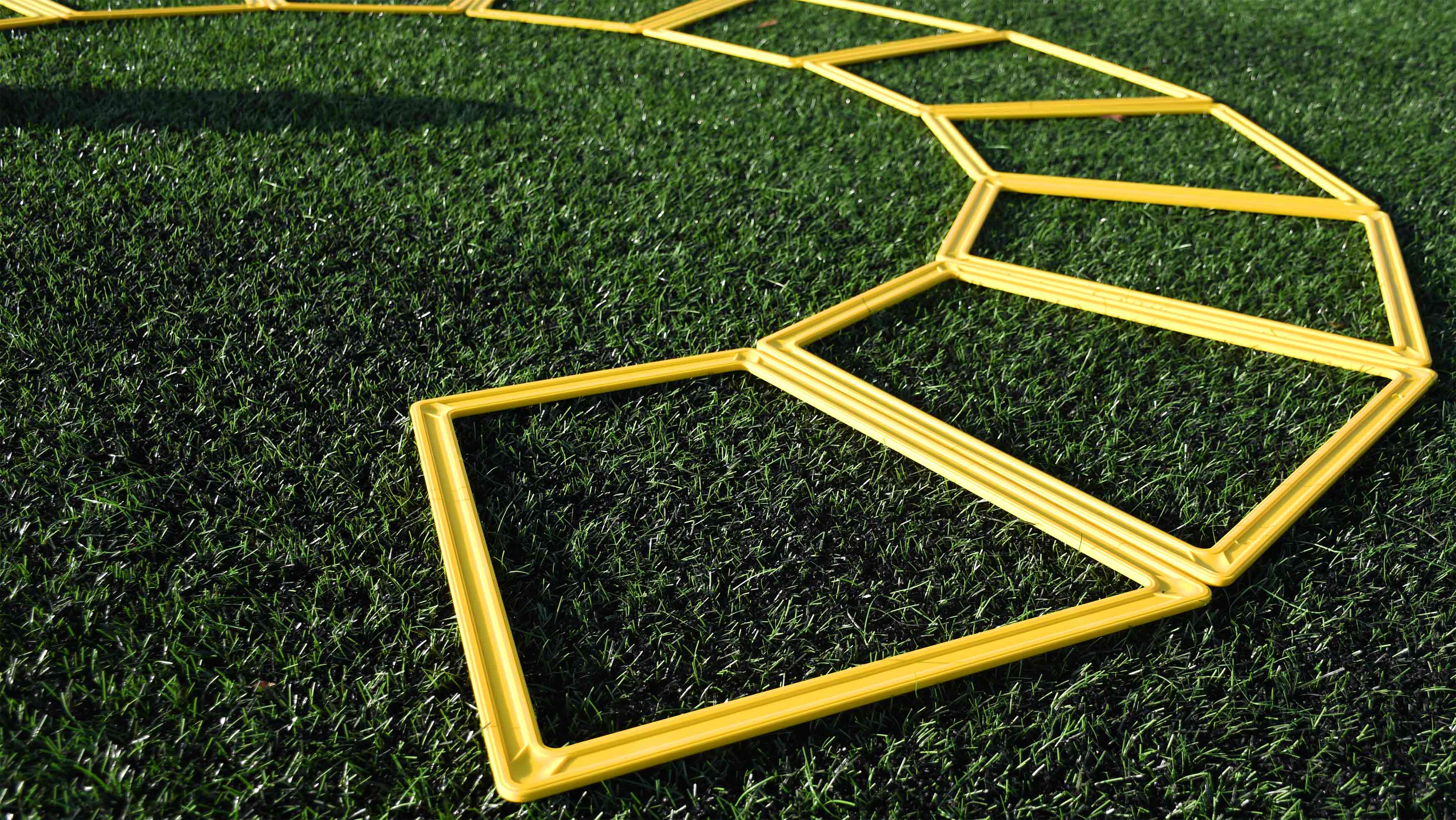 Precision Training’s Precision Poly Grid System (set of 10) features yellow plastic agility grids arranged in a zigzag pattern on green artificial grass, ideal for agility training and enhancing footwork skills.