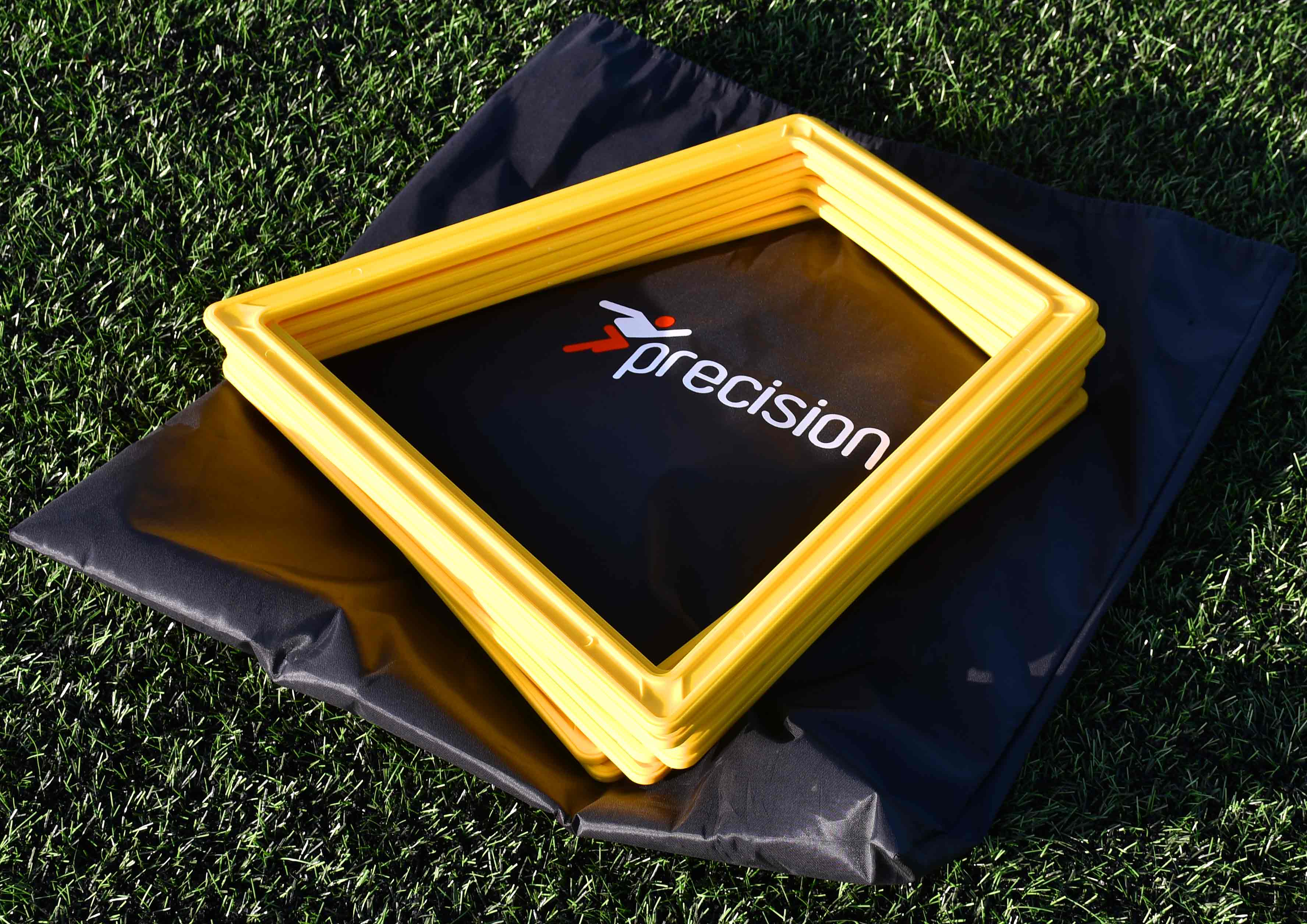 A stack of yellow Precision Training Poly Grid System markers (set of 10) rests on a black branded carrying bag, placed atop green artificial turf.