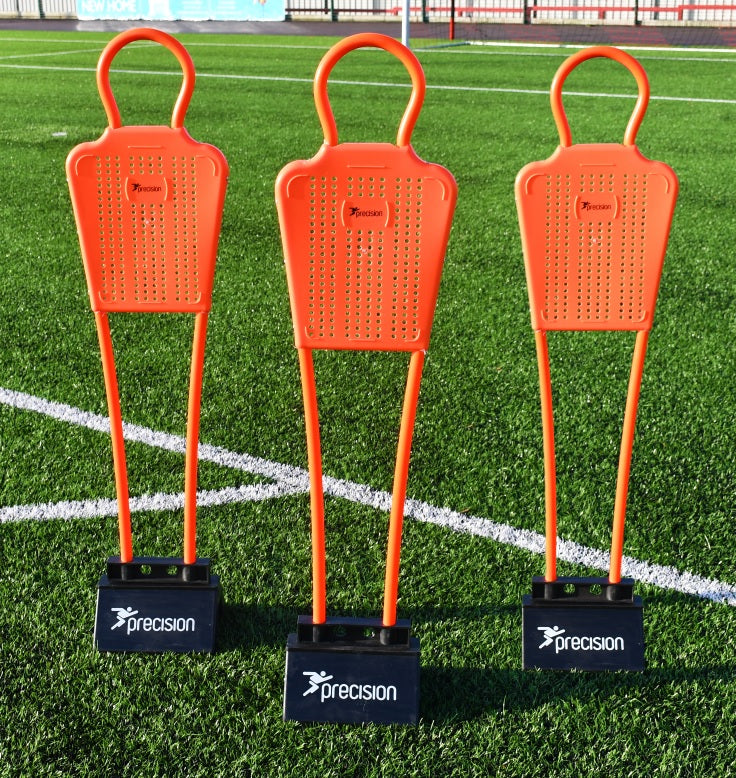 The Precision Training Mini Mannequins (set of 3) feature orange figures with black bases, standing on artificial grass with white field lines—ideal football training equipment for free kick practice.