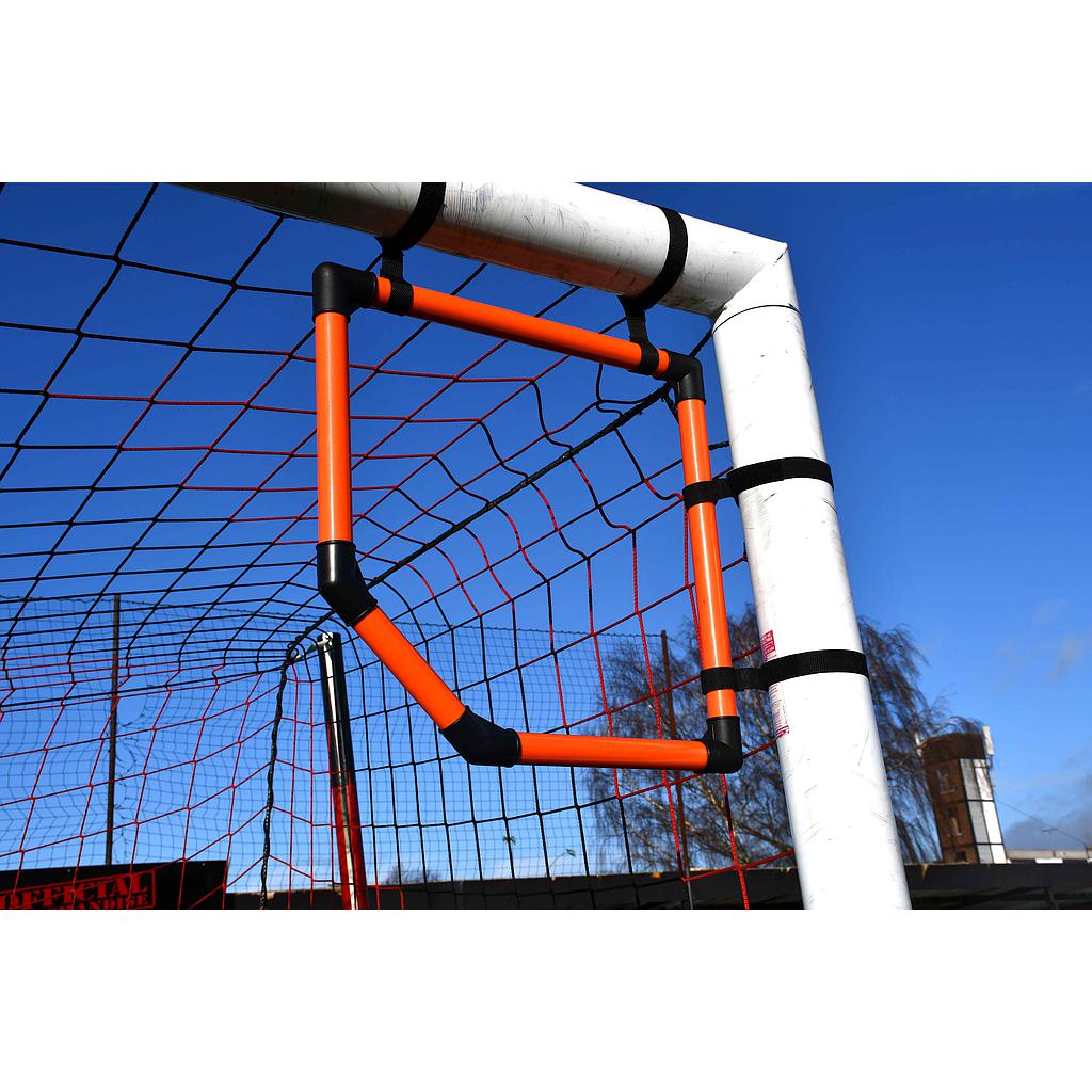 The Precision Training Precision Top Bins Corner Target, in orange and black, is attached to a white soccer goalpost to improve shooting accuracy. Red netting and a clear blue sky are visible in the background.