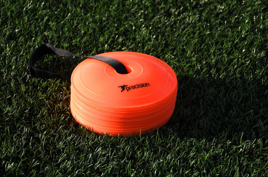 A stack of bright orange Precision Pro Near Flat Markers by Precision Training with a black handle rests on green artificial grass. The top cone features the brand logo, making this set of 40 ideal for soccer training drills.