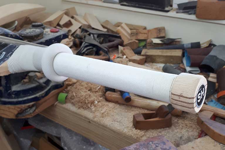 A close-up of a partially completed katana handle wrapped in white cord, resting on a workbench—demonstrating precision similar to Martin Berrill Sports’ Cricket Bat Replacement Grip fitting service.