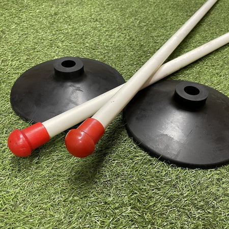 Four Sure Shot Wooden Rounders Posts with red safety caps are shown crossed on artificial grass, alongside two heavy-duty black rubber bases. The equipment is branded Sure Shot and is ideal for sports or training use.