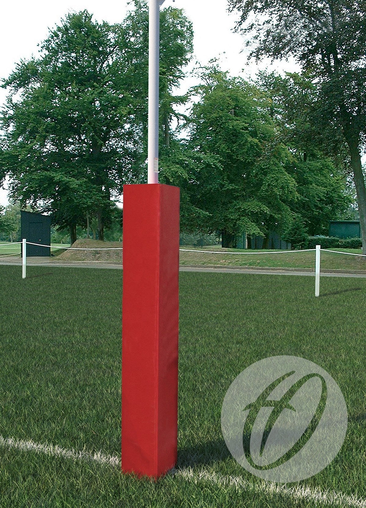 A Harrod Sport Single Colour Club Rugby Post Protector, 254mm, in red, is fitted to a white pole on a grassy sports field with trees and barriers in the background.