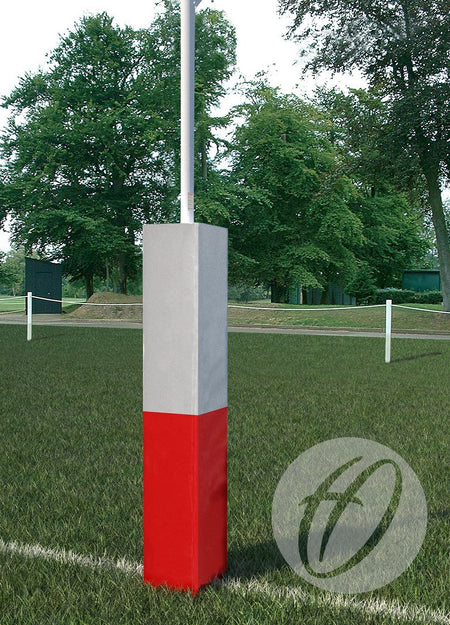 The Harrod Sport Two Panel Club Rugby Post Protector (355mm), featuring a red lower half, gray upper half, and high-density foam, stands on a grassy field bordered by trees and white boundary markers.