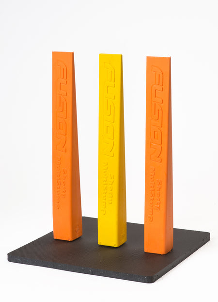 Three tall, triangular Fusion stumps—two orange, one yellow—stand upright on a black Fusion Multi-Stump All Weather Base. Each stump is labeled “FUSION” vertically, perfect for hard wicket or all-weather cricket setups.