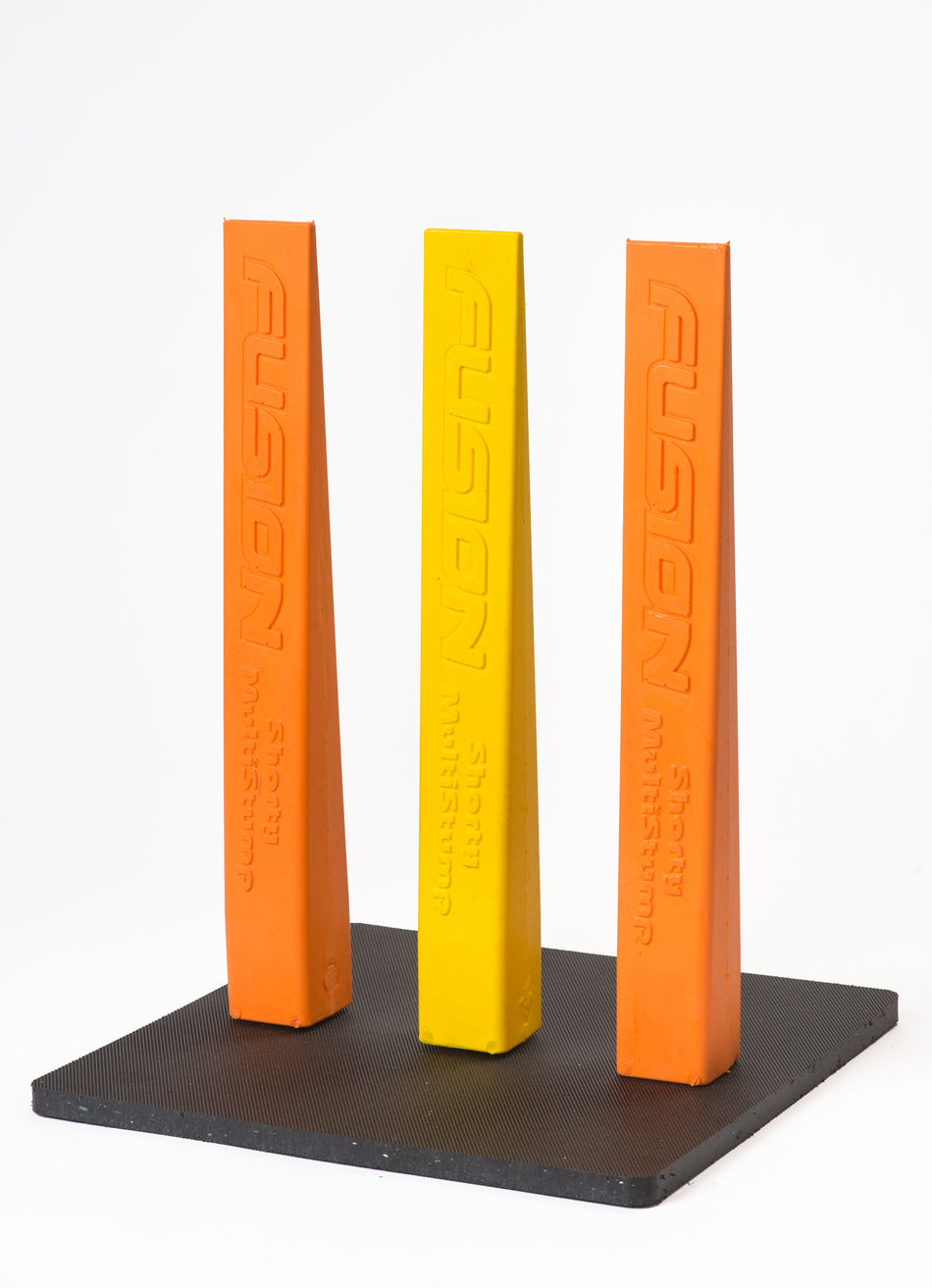 Three tall, triangular Fusion stumps—two orange, one yellow—stand upright on a black Fusion Multi-Stump All Weather Base. Each stump is labeled “FUSION” vertically, perfect for hard wicket or all-weather cricket setups.