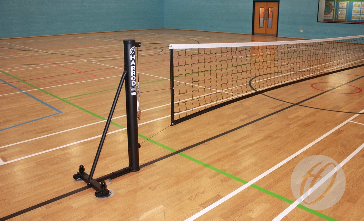 Harrod Sport Sitting Volleyball Posts are set up in an empty indoor gym with a wooden floor, painted court lines, blue walls, double doors, and colorful posters in the background.