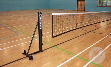 Harrod Sport Sitting Volleyball Posts are set up in an empty indoor gym with a wooden floor, painted court lines, blue walls, double doors, and colorful posters in the background.