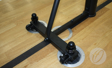 Close-up of the base of Harrod Sport Sitting Volleyball Posts secured to a wooden floor with metal anchors; black bolts and brackets are visible on the support frame, which features an aluminium extrusion for added durability.