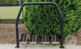 A Harrod Sport Socketed Angle Boot Wipers unit with black metal frame and beech timber brushes is installed outdoors on concrete, positioned in front of green bushes and a wire fence.