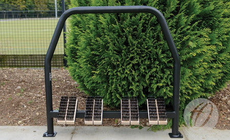A Harrod Sport Socketed Angle Boot Wipers unit with black metal frame and beech timber brushes is installed outdoors on concrete, positioned in front of green bushes and a wire fence.