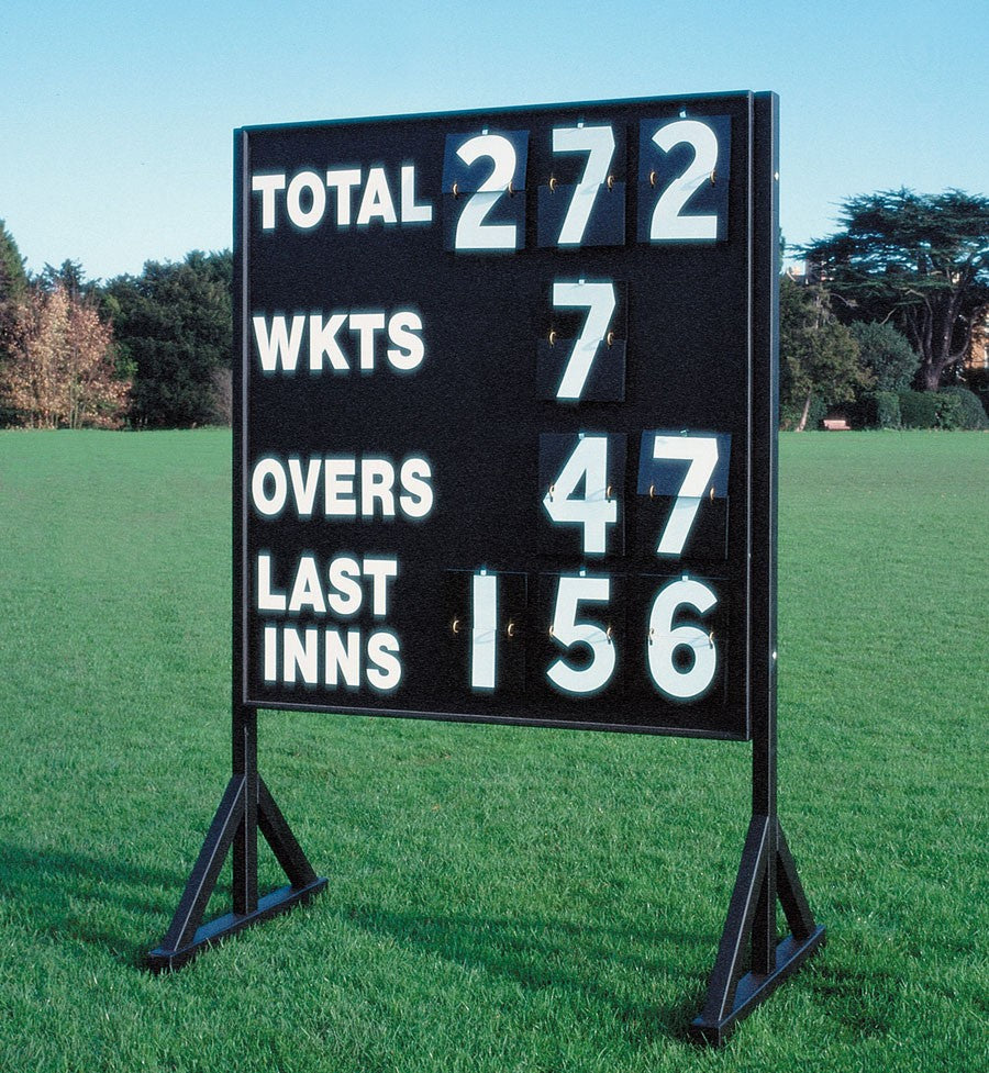 A Martin Berrill Sports Standard Cricket Scoreboard stands on grass, showing Total 272, Wickets 7, Overs 47, Last Innings 156. Trees and blue sky appear in the background.