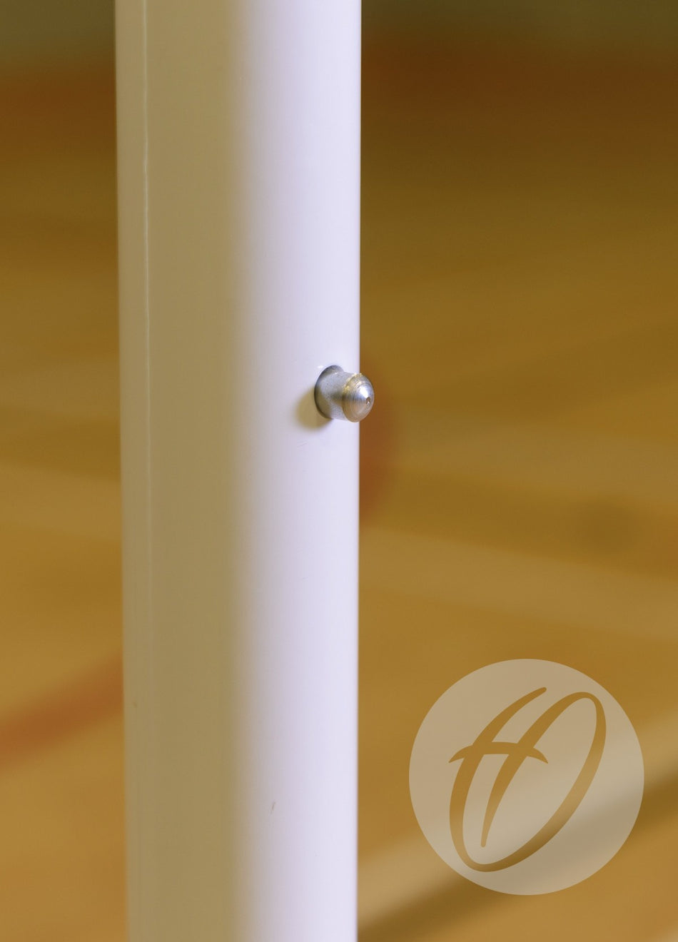 A close-up of the Harrod Sport Single Telescopic Netball Post, made from lightweight aluminium with a small silver bolt, set before a blurred brown and beige background. A partially visible circular logo appears at the bottom right.