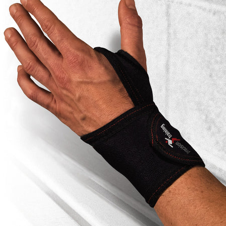 A person wears a Precision Training Precision Neoprene Thumb/Wrist Wrap, a black adjustable brace with red stitching and logo, designed for wrist pain relief and support, shown with their hand open against a light background.