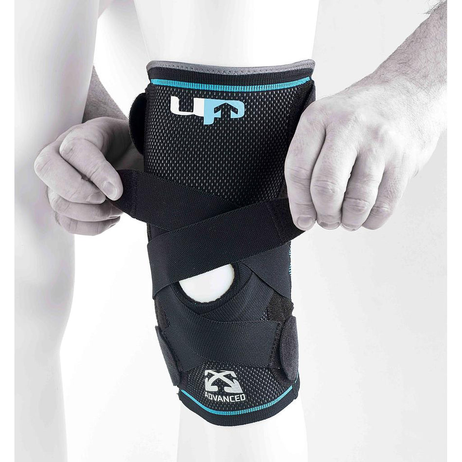 A person adjusts the Reydon Sports Ultimate Performance Advanced Ultimate Compression Knee Support, a black brace with straps and an open patella design, offering stability, comfort, and visible branding.