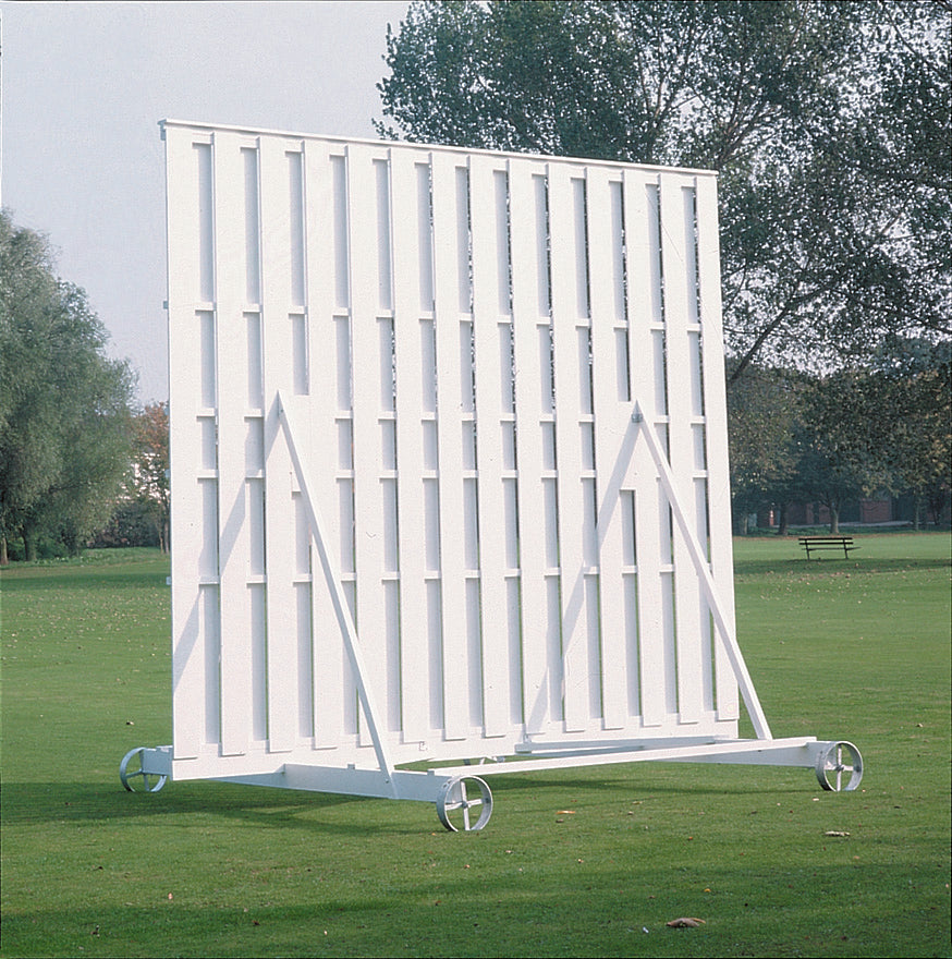 The Martin Berrill Sports Wooden Sight Screen 3.66m x 3.66m, featuring wheels, is positioned on a grassy field with trees and a park bench in the background.
