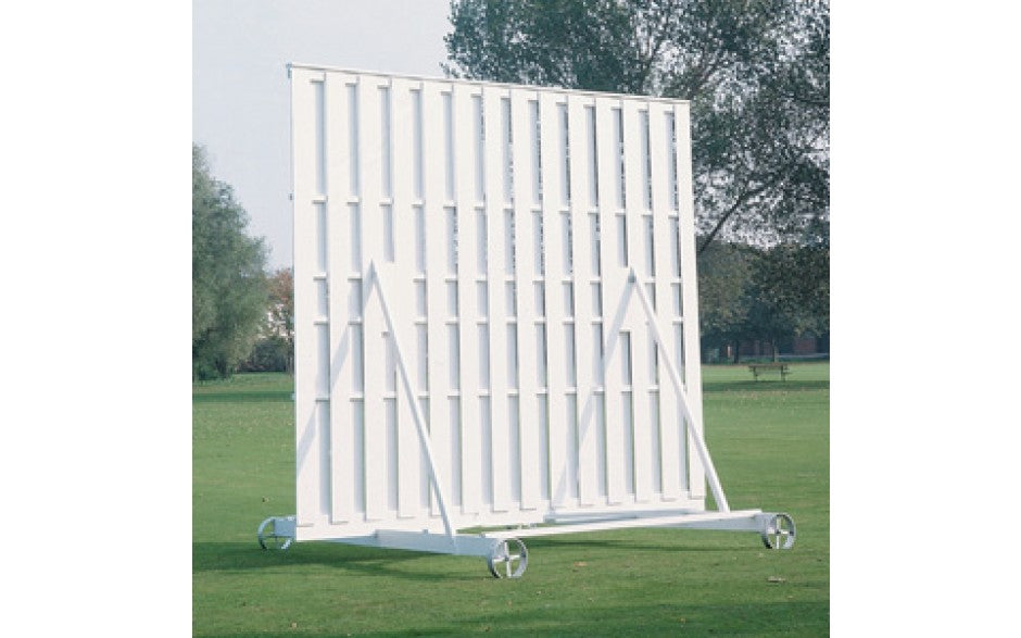 The Martin Berrill Sports Wooden Sight Screen 3.66m x 3.66m, mounted on wheels, stands on a grassy field with trees and a clear sky in the background.