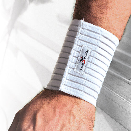 A close-up of a forearm wearing the Precision Training Precision Elasticated Wrist Wrap - Universal in white, featuring ribbed material, adjustable compression, and a small X Training logo patch. The background is blurred and mostly white.